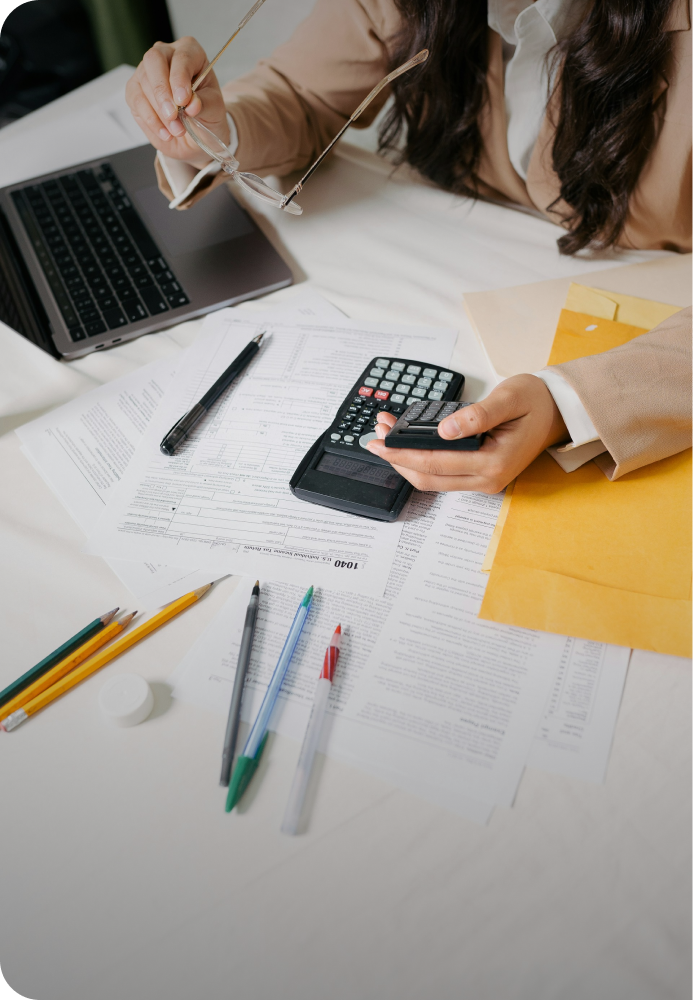 Camera shot of a table and a woman looking at a calculator, deciphering an undisclosed amount.