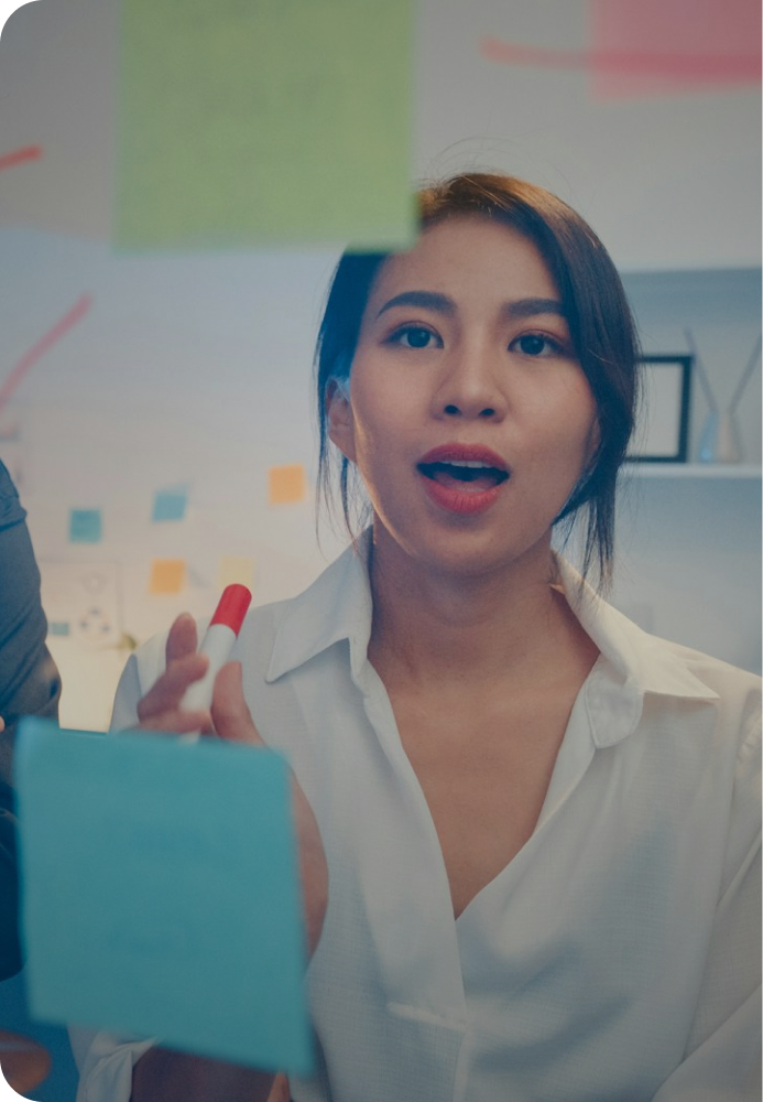 A woman in mid thought, trying to brainstorm with sticky notes on a glass wall. 