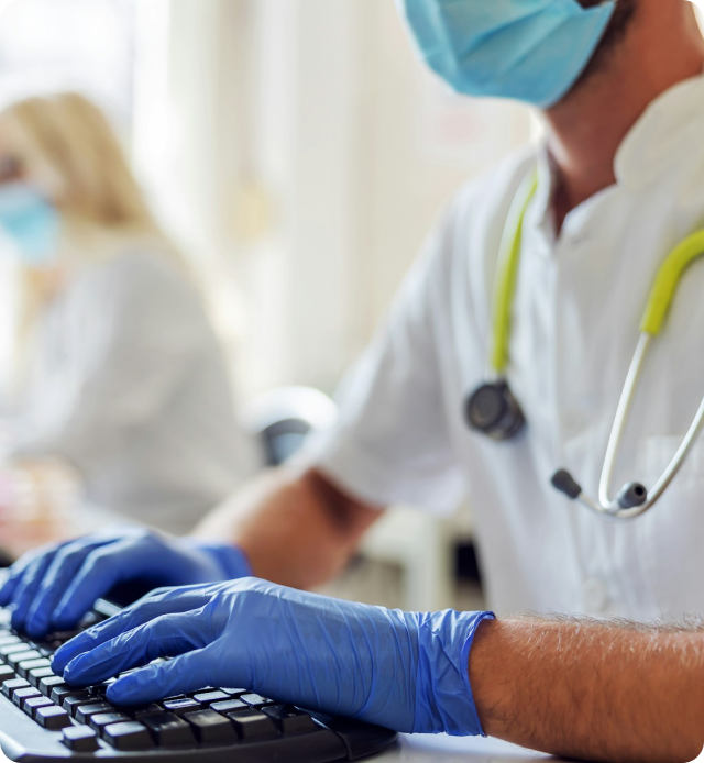 Physician with rubber gloves at computer, looking up data to make informed decisions.