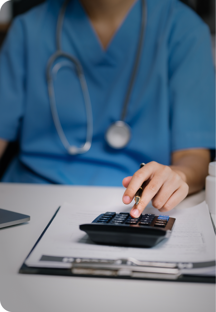 A physician sitting down to do some paperwork, while also typing something in on their calculator.